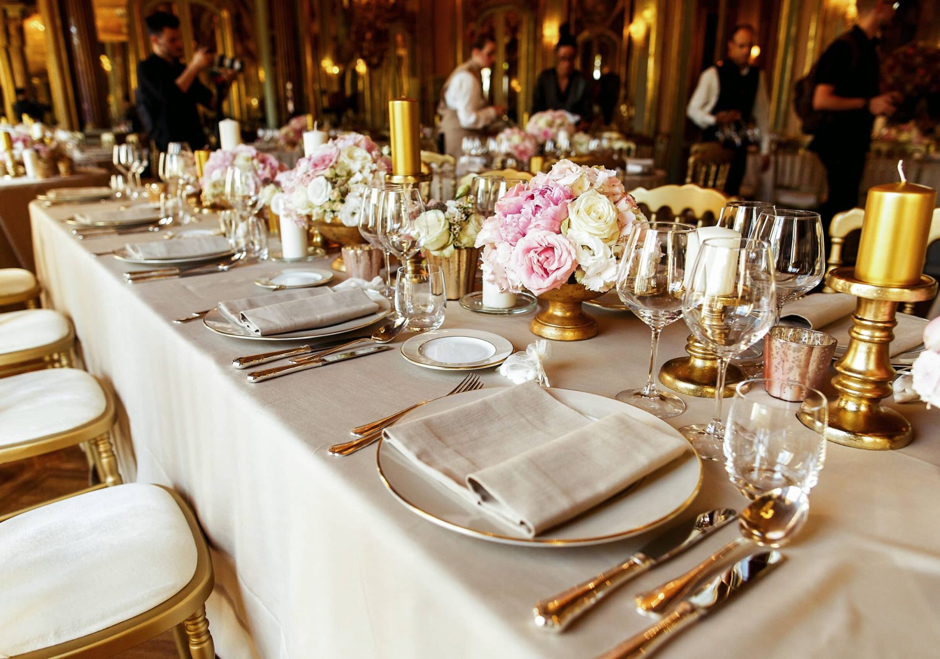 Look from afar at dinner table served with rich cutlery and crockery, golden vases and candleholders